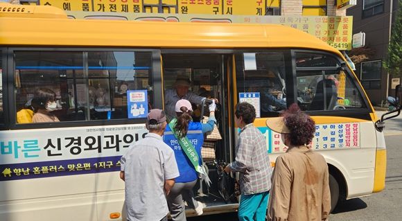 발안 만세시장 앞 정류장에서 승하차 안전도우미 활동을 수행한 HU공사 임직원이 어르신의 무거운 짐을 들어주고 있다.(화성도시공사 제공)