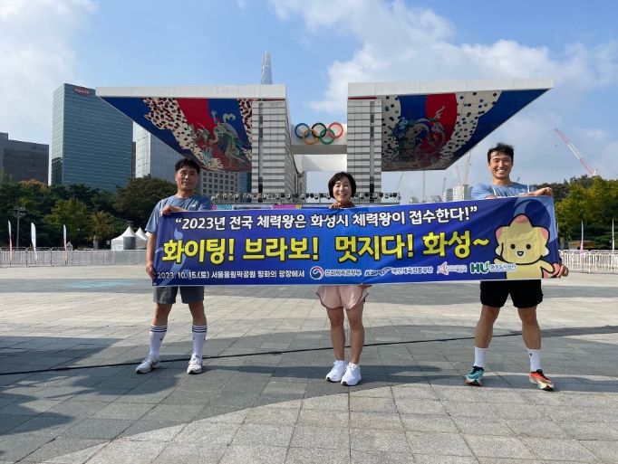 올림픽공원 평화의 광장 앞에서 화성시 체력왕 대표로 전국대회에 참여한 시민 3명이 현수막을 사진을 찍고 있다. (화성도시공사 제공)