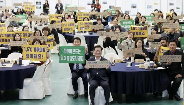 박승원 광명시장이 2024년 11월 광명남초등학교를 방문해 초등학생들과 광명시의 탄소중립 정책에 대해 소통하고, 자신만의 탄소중립 실천 방법을 작성한 종이를 들고 기념사진을 촬영하고 있다.